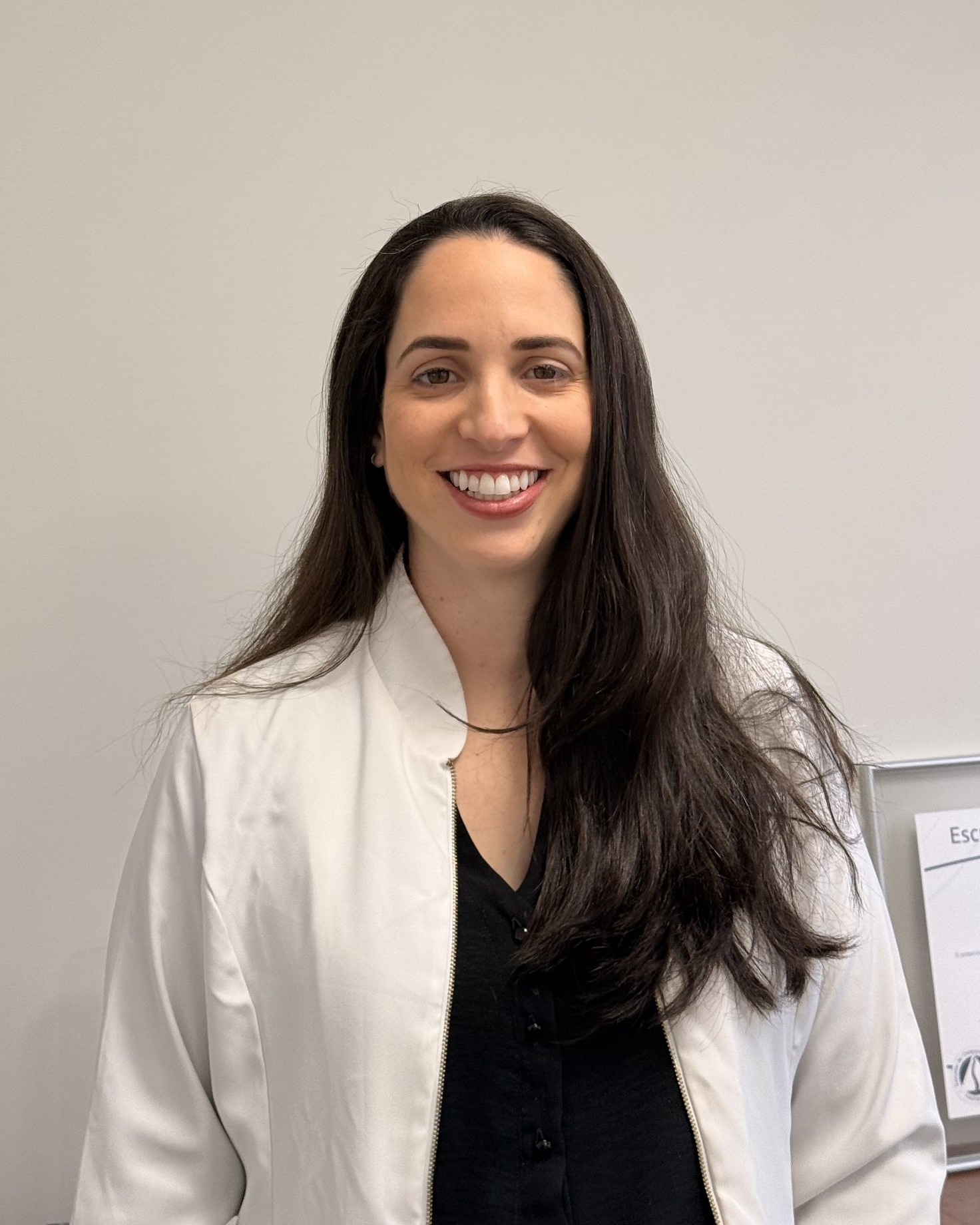 Paula Mantovani sorrindo, de jaleco, no consultório